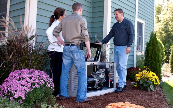 A generator maintenance man showing two customers the inside of their generator